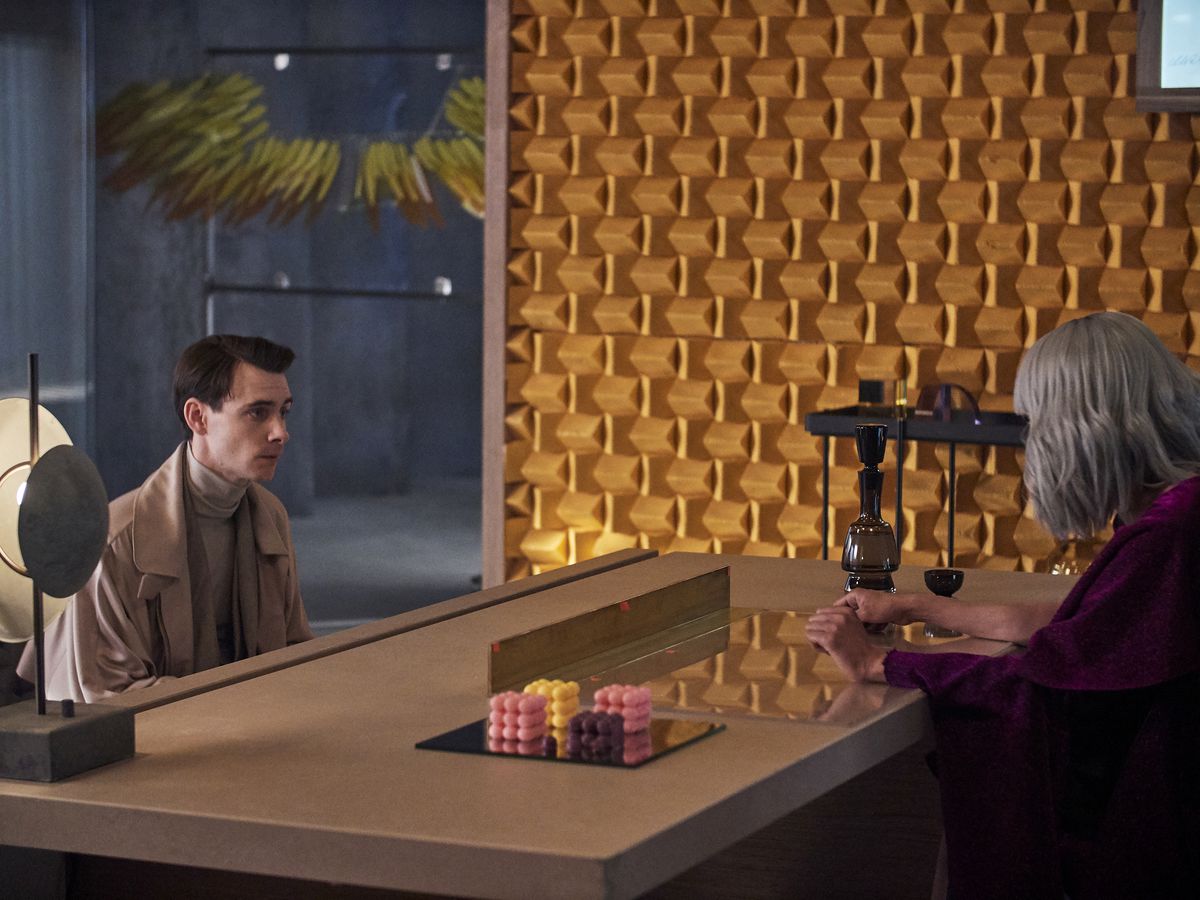Harry Lloyd, apparentemente nervoso, si siede di fronte a un ampio tavolo di Hannah John-Kamen in Brave New World.