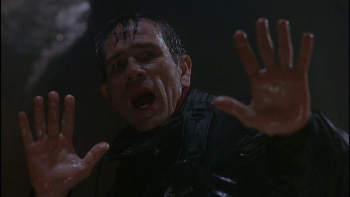 Un uomo inzuppato d'acqua alza le mani.