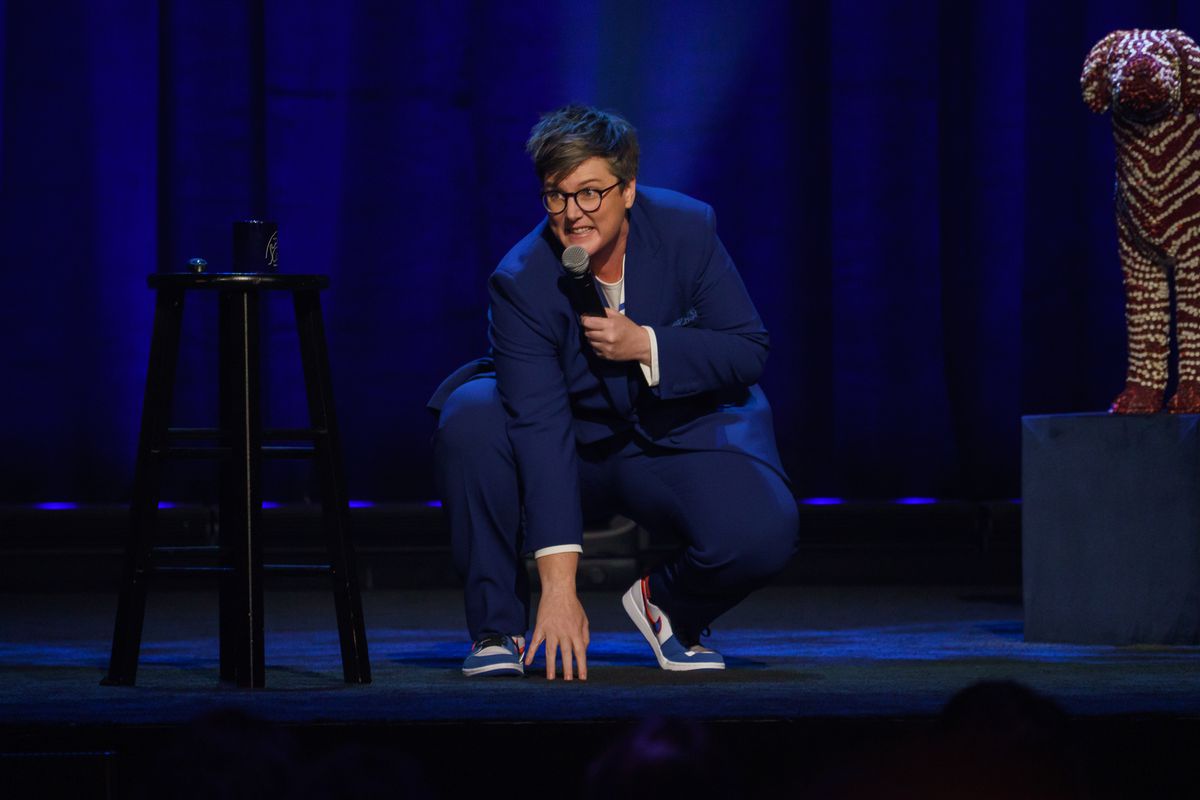 Hannah Gadsby si accovaccia per toccare il pavimento con un microfono in mano a Douglas