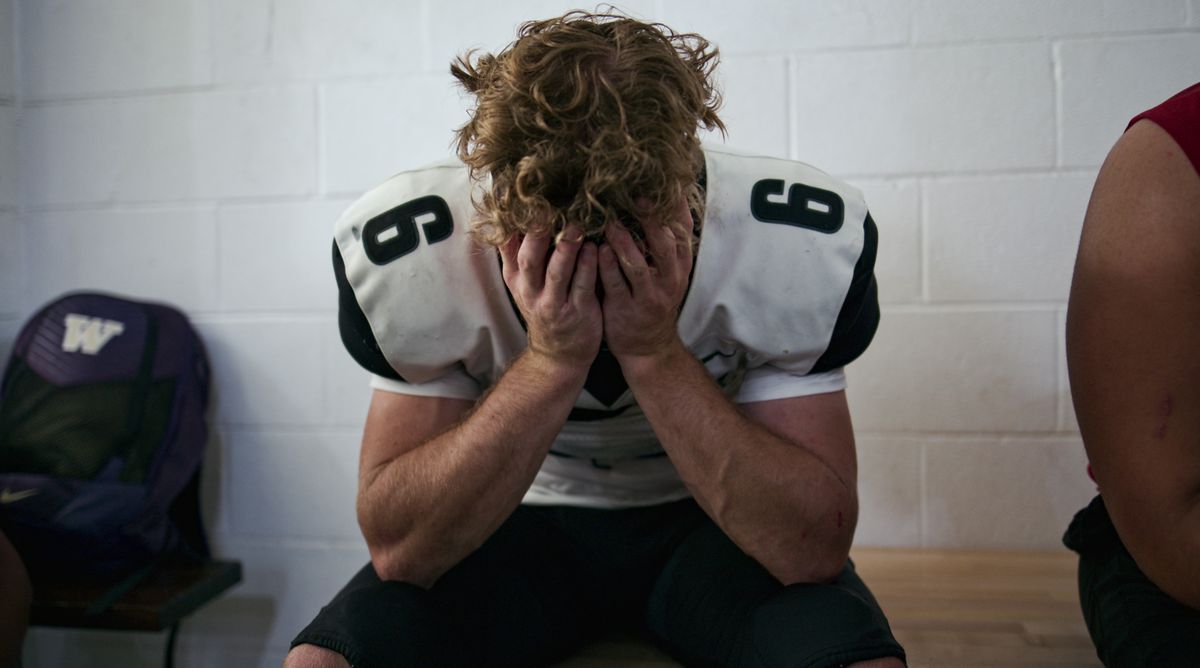 Un giocatore di football in uniforme si accascia sulla panchina con la testa tra le mani in Last Chance U: Laney