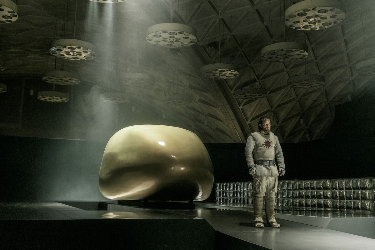 Travis Fimmel è in piedi accanto a un'elegante capsula spaziale in uno strano hangar spaziale in Raised By Wolves.