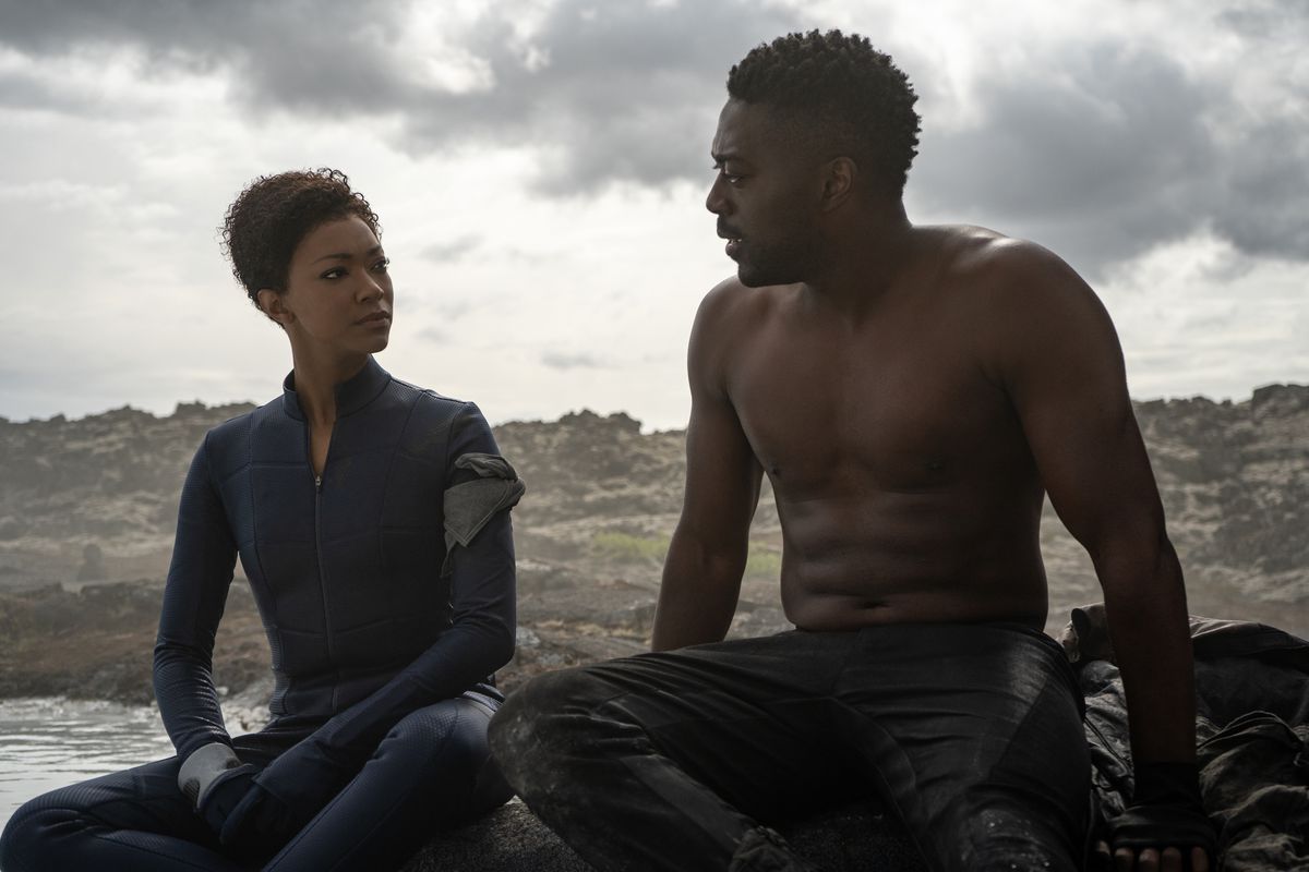 Sonequa Martin-Green siede accanto a David Ajala a torso nudo in un paesaggio arido sull'acqua in Star Trek: Discovery