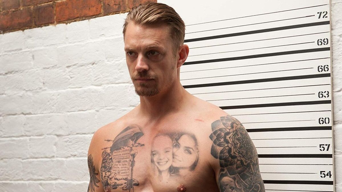 Un Joel Kinnaman senza maglietta e pesantemente tatuato si trova davanti a un muro con la misurazione dell'altezza in The Informer