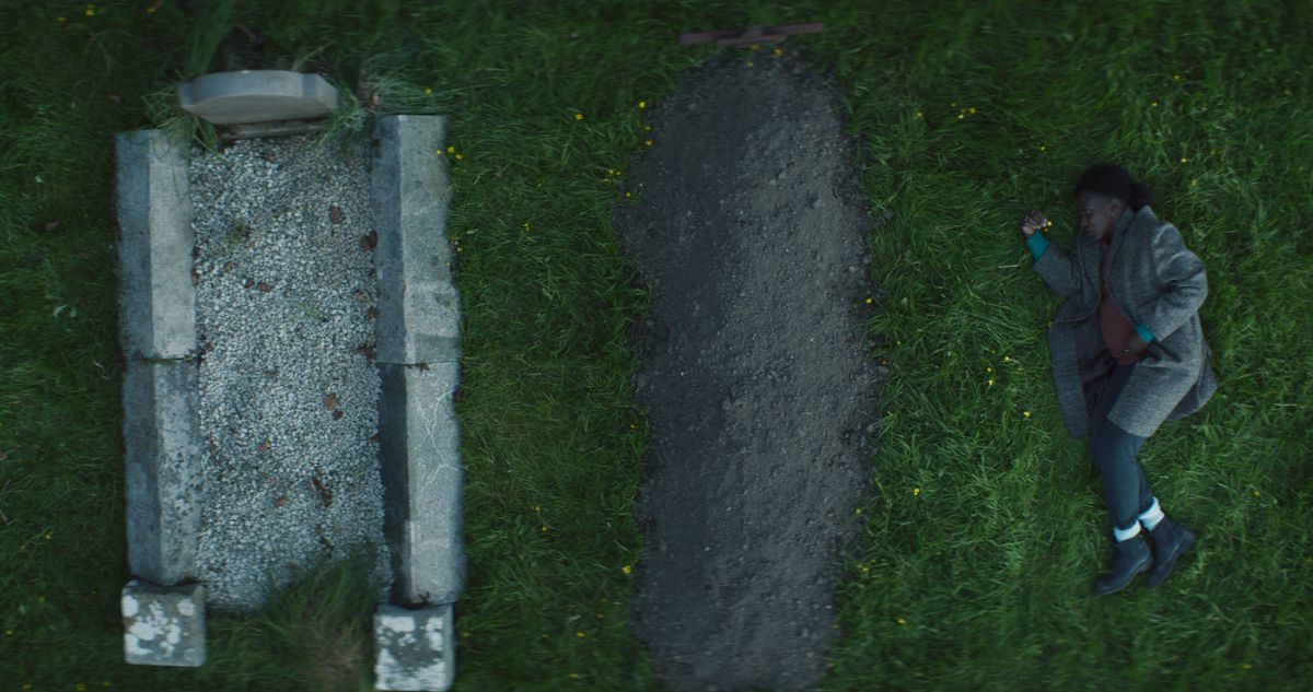 Una donna molto incinta (Tamara Lawrance) giace sull'erba accanto a due tombe a Kindred