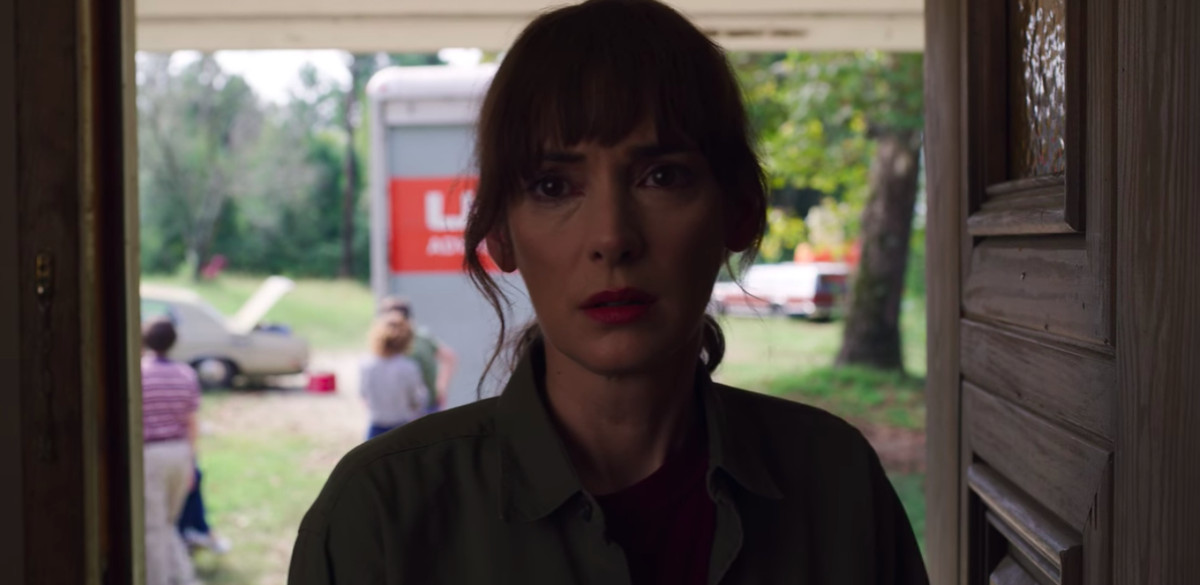 Una donna si trova nel telaio di una porta e guarda con desiderio la telecamera.