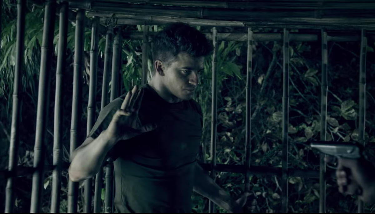 un POW muscoloso alza la mano sotto la minaccia di una pistola per offrirsi volontario per una lotta all'ultimo sangue