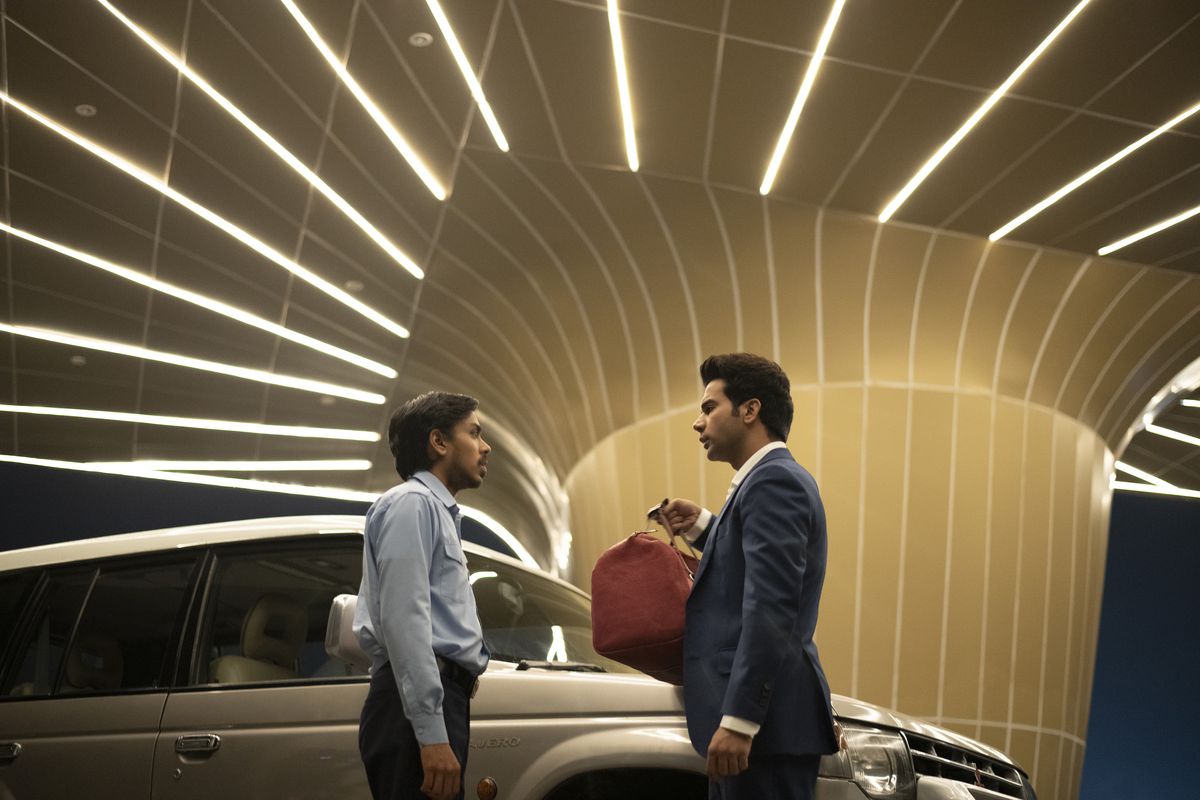 Adarsh Gourav e Rajkummar Rao si affrontano sotto un posto auto coperto a strisce di luci al neon in The White Tiger.