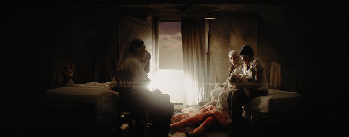 Quattro donne in una stanza buia si radunano intorno al corpo insanguinato di una donna che ha appena partorito in The Wanting Mare