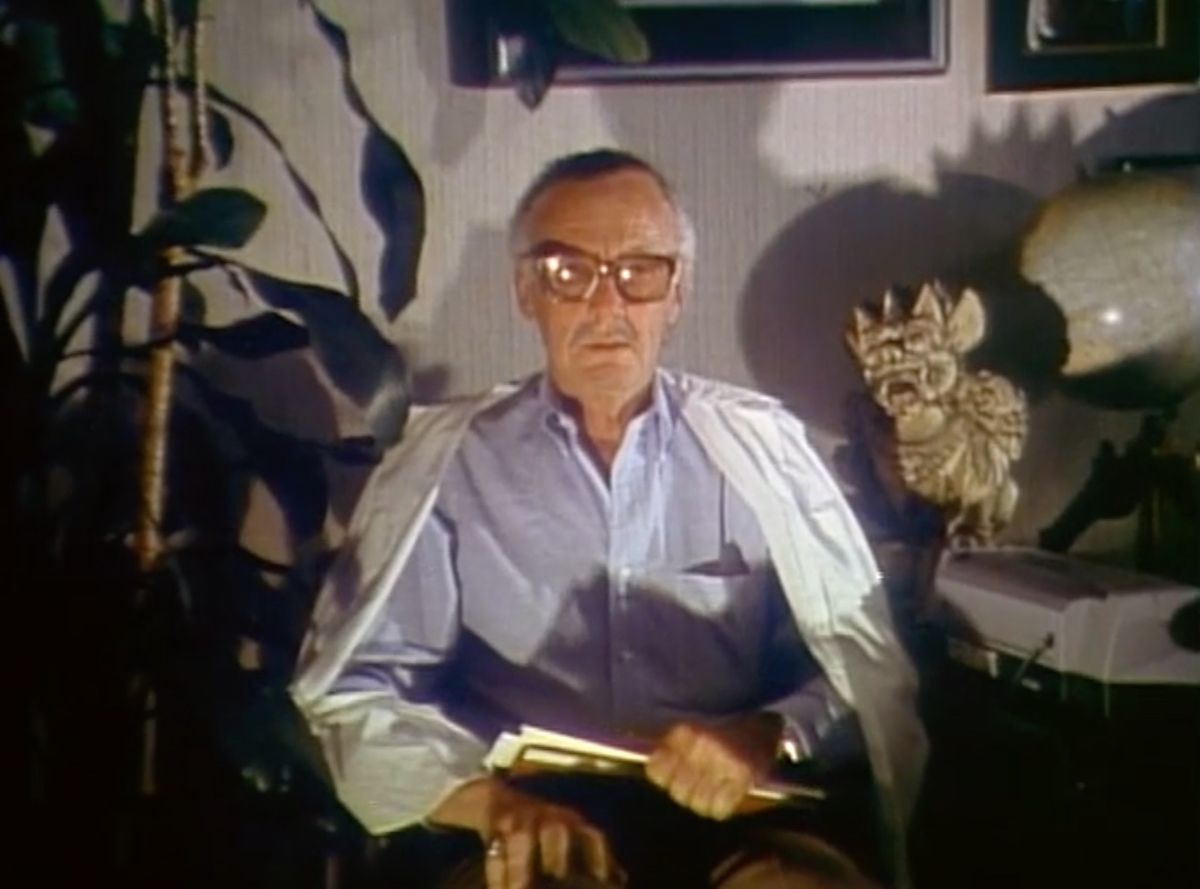 Stan Lee sitting in a chair with a book on his lap in Jugular Wine: A Vampire Odyssey (1994)