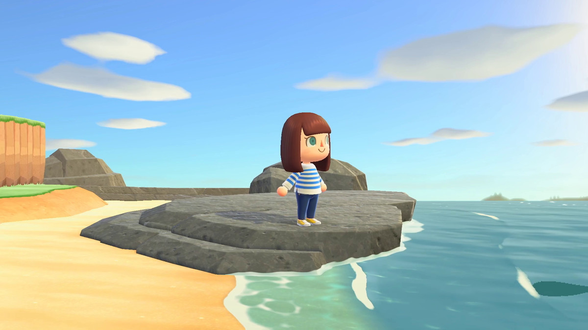 a brown-haired woman in a blue-and-white striped shirt and blue jeans stands on a stone platform on a beach in Animal Crossing: New Horizons