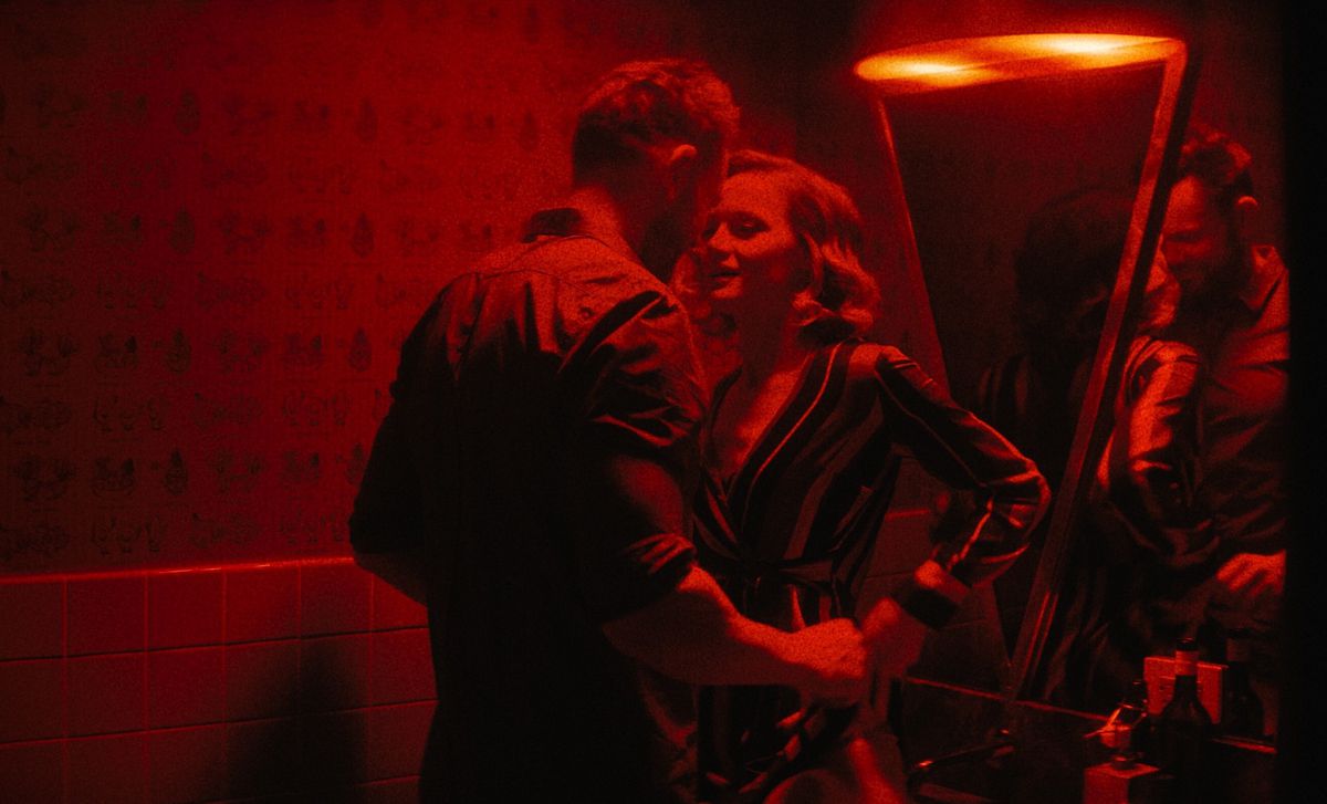 Sotto luci rosse fioche, Joel McHale e Kerry Bishé si baciano in un bagno in Happily