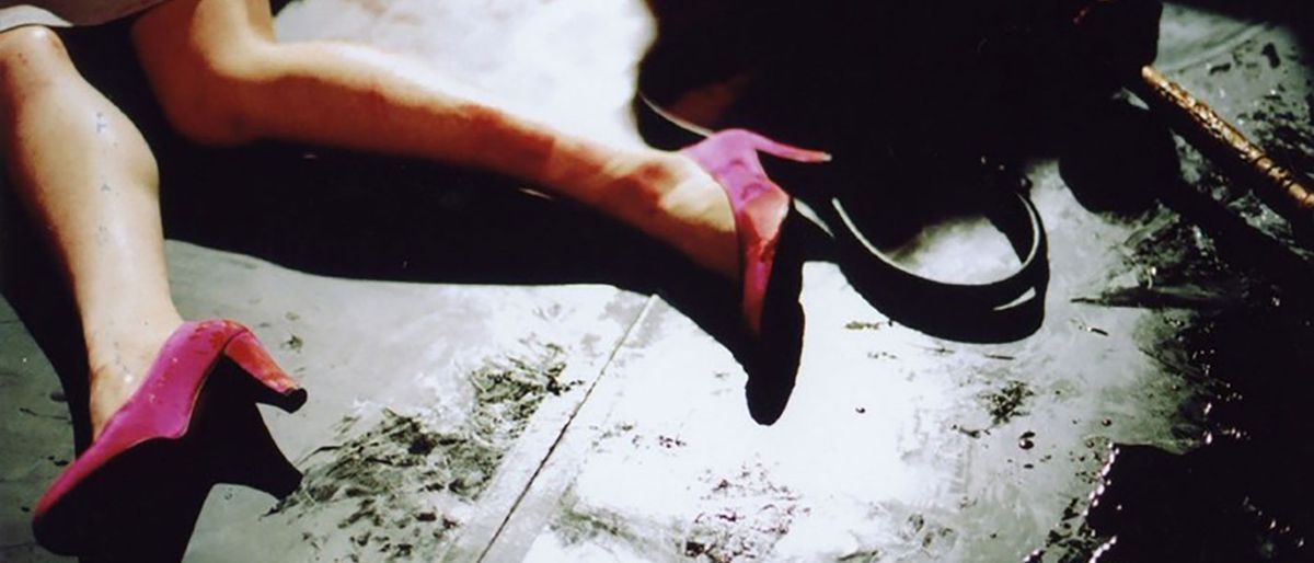 Le gambe e le caviglie del corpo di una donna distesa con indosso tacchi alti che onestamente sembrano molto più rosa che rossi in The Red Shoes