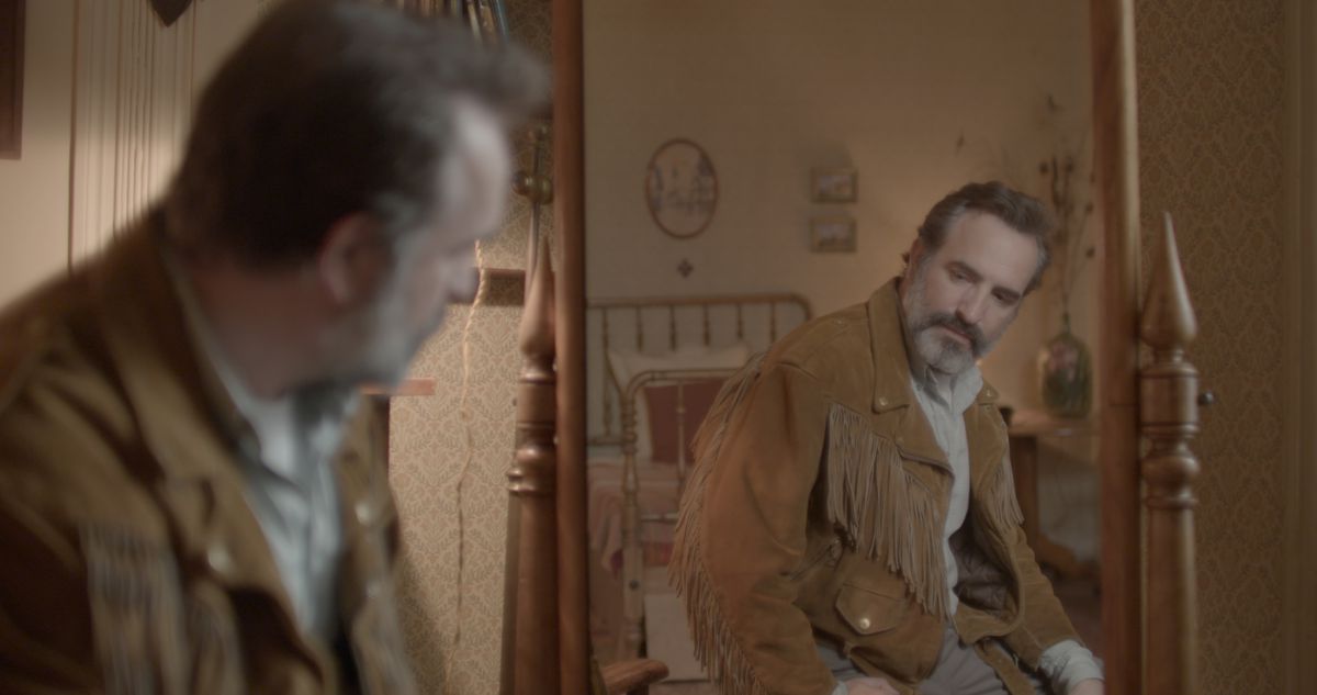 Un uomo con una giacca di camoscio con frange si guarda di traverso nello specchio in pelle di daino