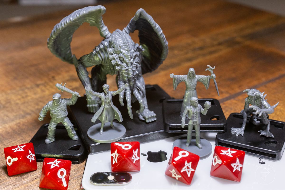 Miniatures of an Elder God and several smaller minions, plus a pair of heroes, standing on an iPhone.