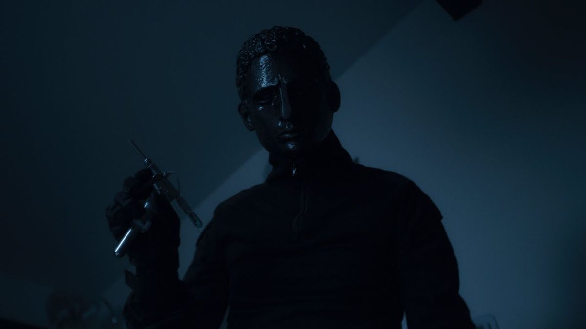 A man in a black metal mask holds a syringe in 2021’s Held