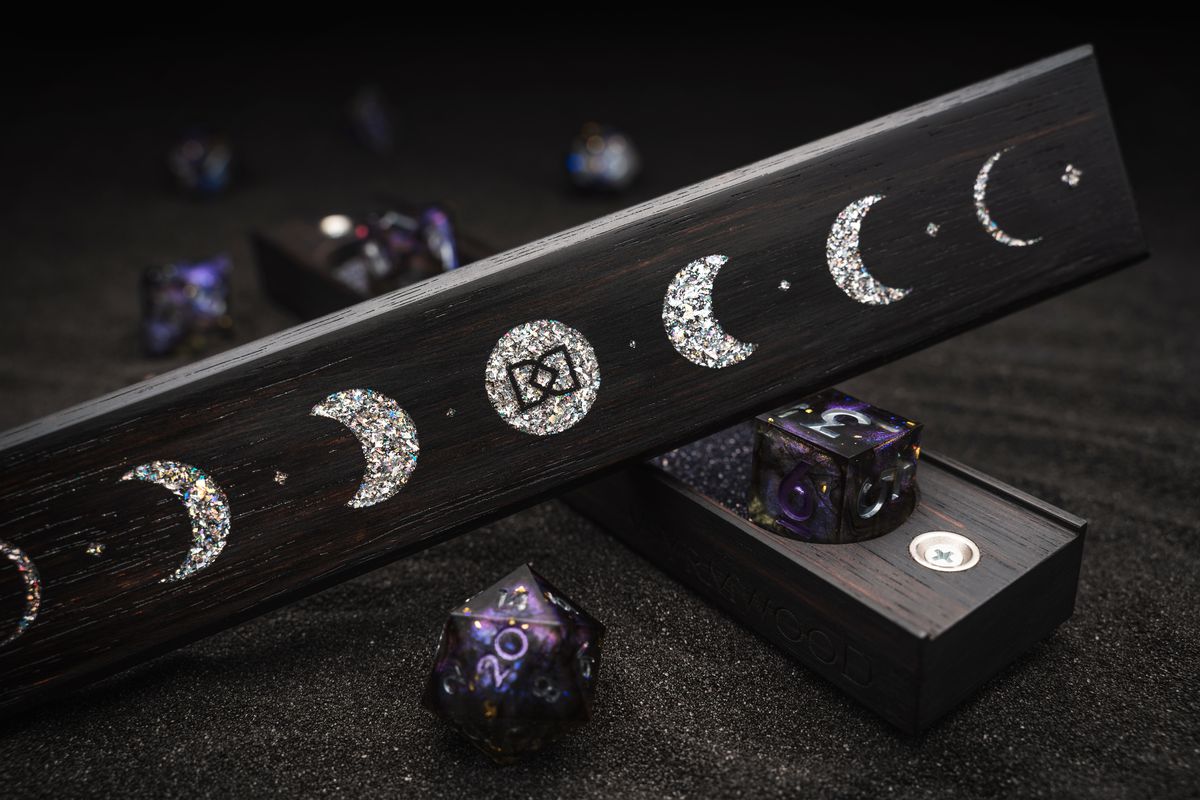 Fasi del motivo lunare, reso in scaglie opalescenti, sostenuto da dadi trasparenti viola e neri.