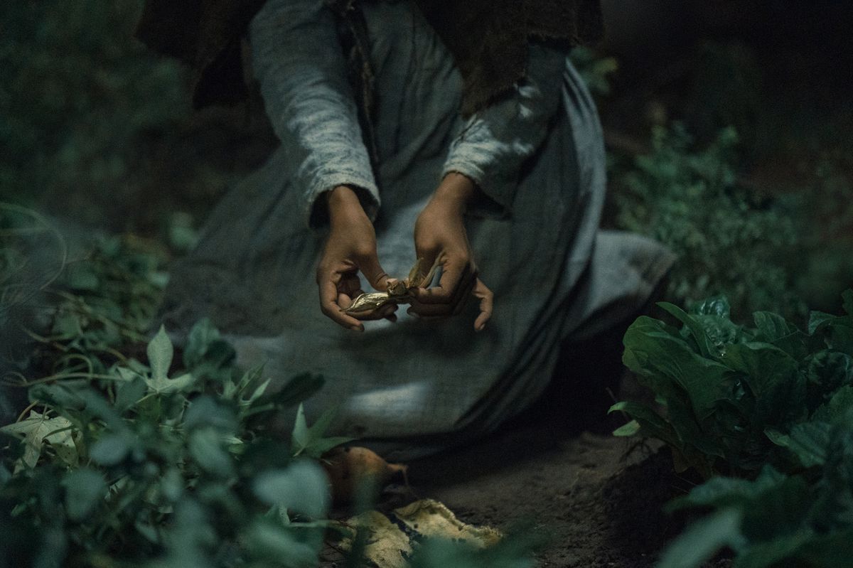 Una donna di colore con un abito ruvido fatto in casa tiene un piccolo oggetto d'oro nella Underground Railroad di Barry Jenkins