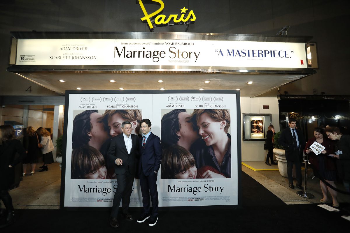 Ted Sarandos and Noah Baumbach stand in front of a Marriage Story movie poster and the Paris Theater marquee which reads “masterpiece”