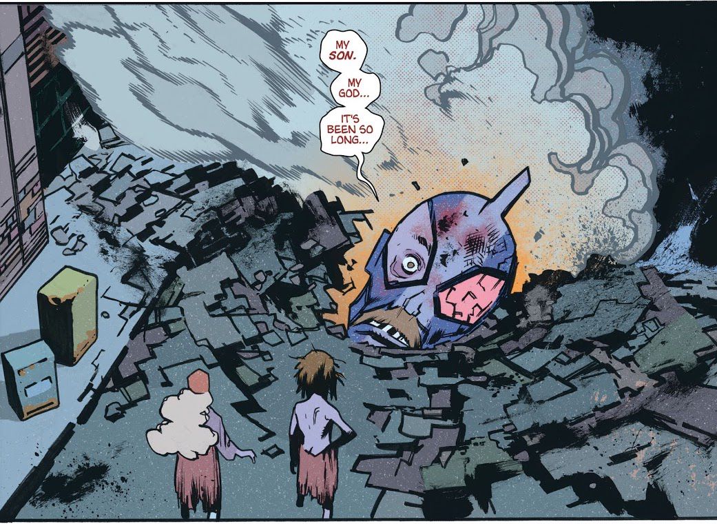 L'enorme testa mozzata di un guerriero kaiju in stile Ultraman - i suoi baffi in stile papà sono visibili nonostante il costume - giace in un cratere in una strada cittadina mentre due persone di taglia normale e vestite in modo stracciato guardano.