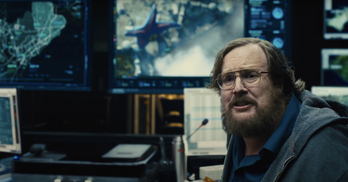 Un uomo in difficoltà siede davanti al monitor di un computer che mostra le riprese satellitari di Starro in The Suicide Squad (2021).