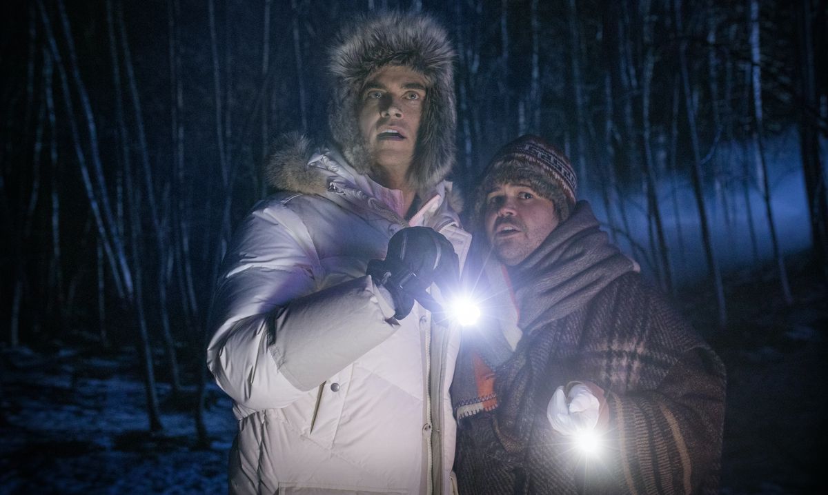 Cheyenne Jackson e Harvey Guillén si stringono insieme all'aperto, impugnando torce elettriche, in Werewolves Within