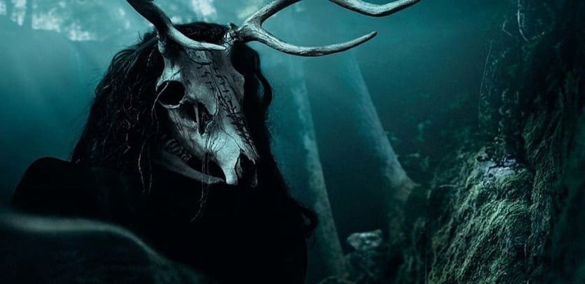 Una figura inquietante con un teschio cornuto al posto della testa e una parrucca nera da spavento si trova nei boschi in una luce blu nella svolta sbagliata del 2021