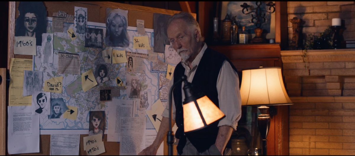 I film di Tobin Bell of the Saw si trovano di fronte a una buona vecchia bacheca di cospirazione piena di mappe, disegni di bambini dagli occhi neri e frecce di post-it in Let Us In