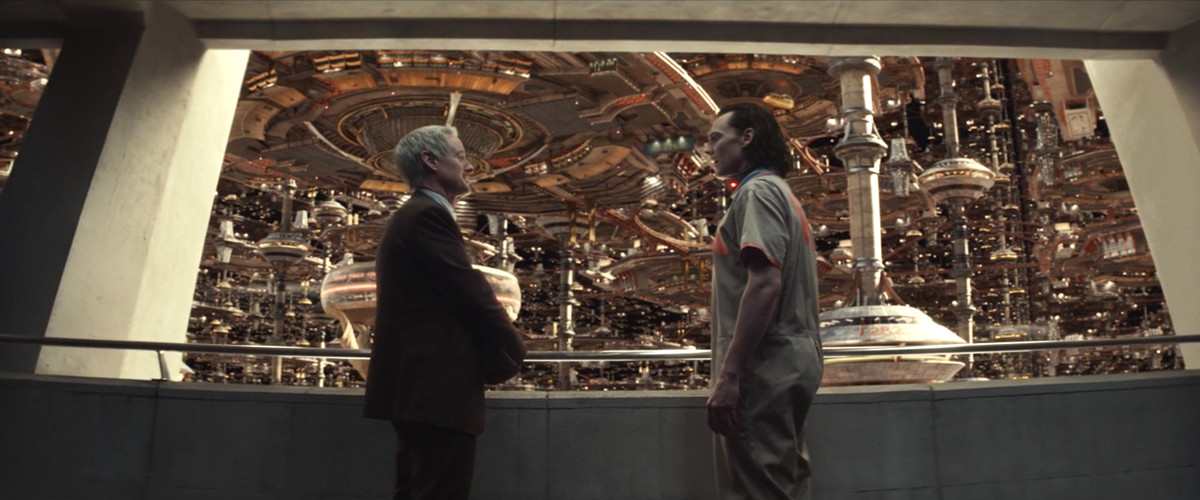 Loki e l'agente Mobius stanno davanti a una finestra brutalista guardando l'enorme cittร /struttura dell'Autoritร per la variazione temporale a Loki.
