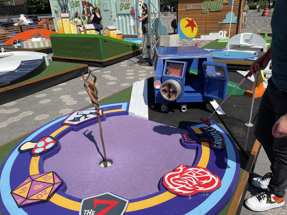 una buca da minigolf che è un furgone che conduce in una sorta di situazione in stile DnD sul fondo con un bastone magico e dadi