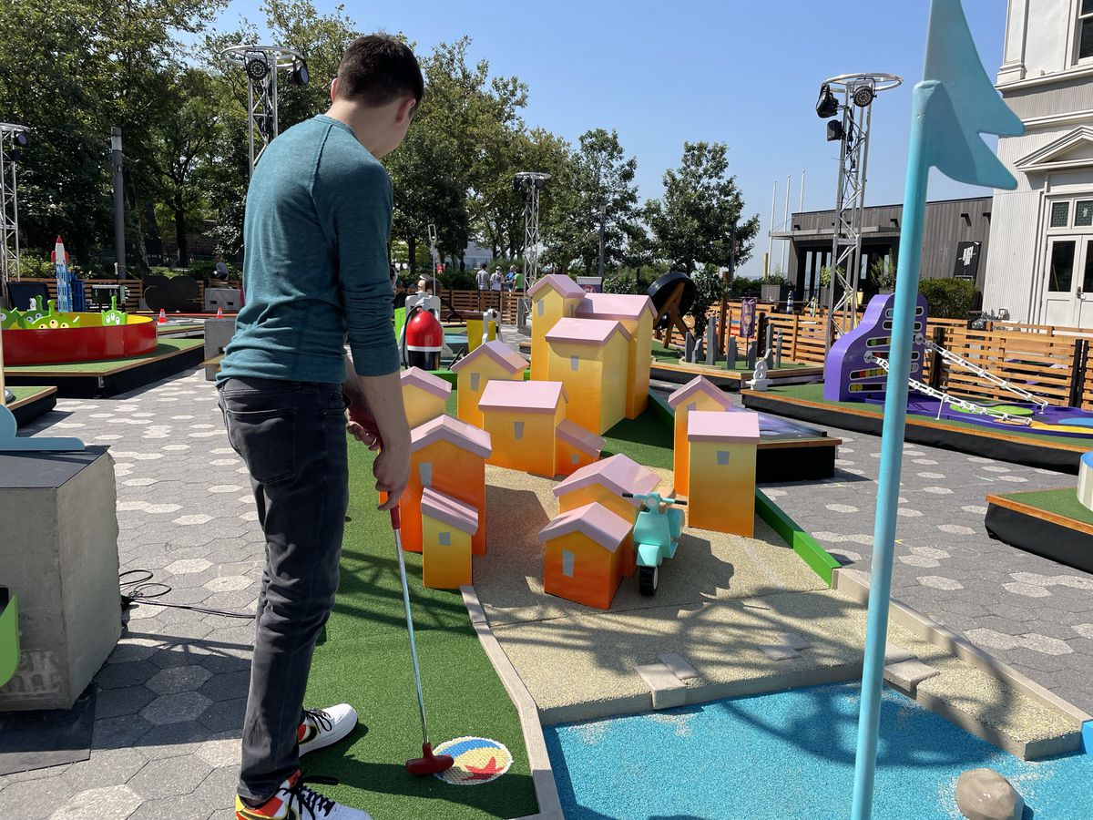 Austen, in qualche modo indossando maniche lunghe e pantaloni lunghi con un tempo di 95 gradi, mette una pallina da golf in un campo progettato per sembrare un'idilliaca cittadina di mare in Italia