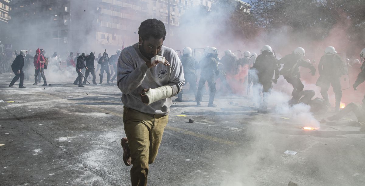 Il protagonista di Beckett, John David Washington, con le mani bendate e insanguinate, corre per le strade piene di fumo mentre sullo sfondo si svolge una rivolta