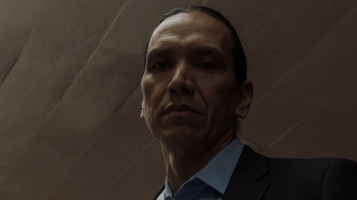 Low angle shot of Michael Greyeyes in a suit looking down in Wild Indian