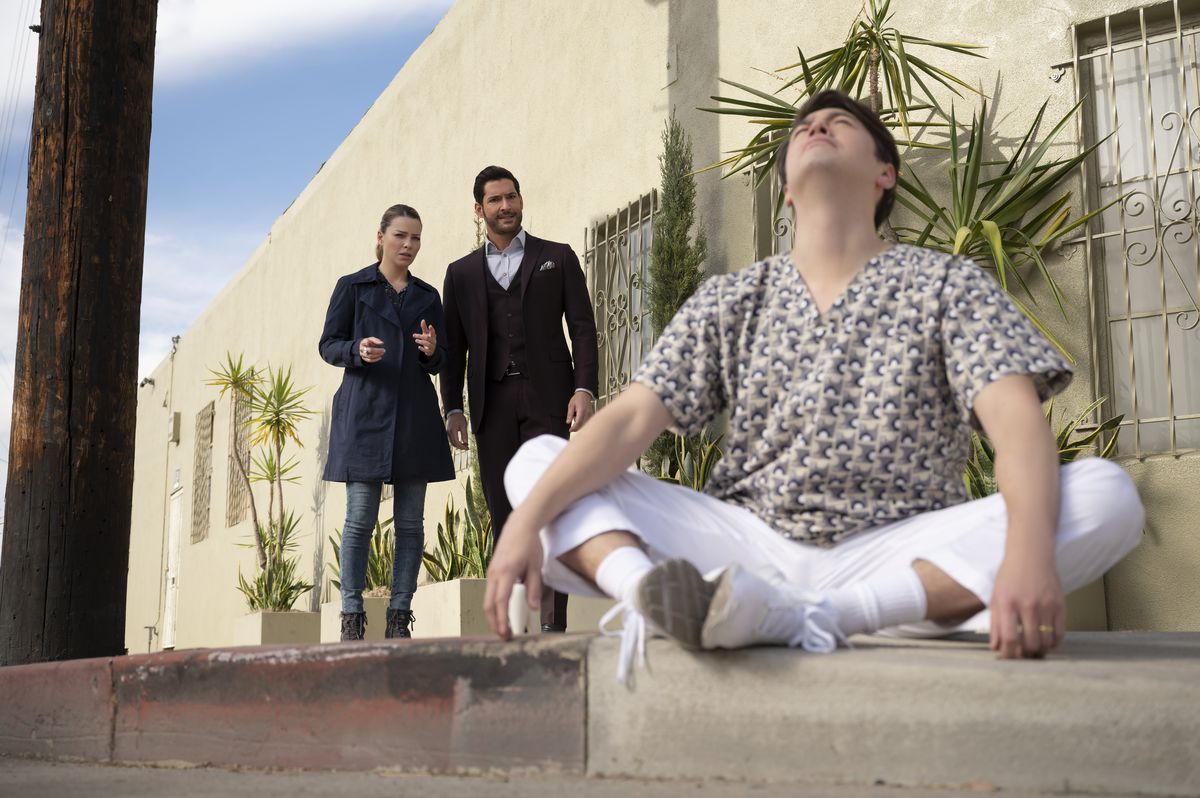 Lauren German e Tom Ellis mentre Chloe e Lucifer si avvicinano a un uomo seduto nella posizione del loto con gli occhi chiusi nella sesta stagione di Lucifer