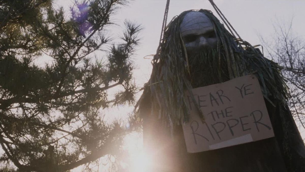 Una macabra effigie mascherata con un cartello di cartone con la scritta