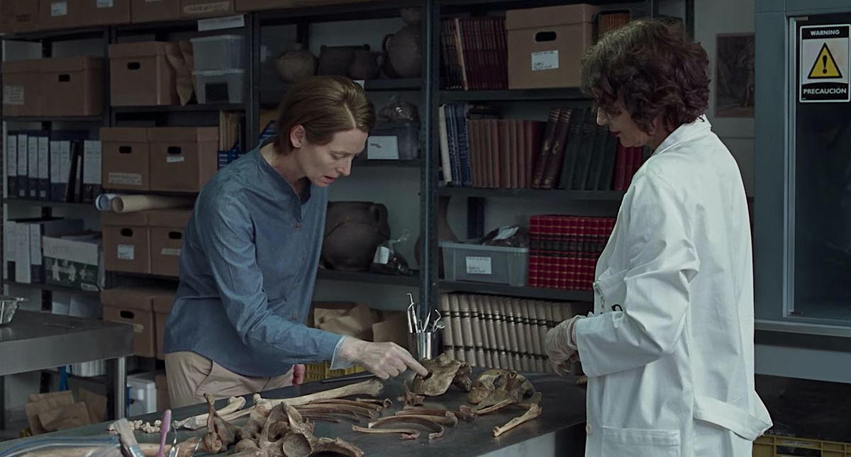 Tilda Swinton e un personaggio rivestito di laboratorio esaminano un mucchio di ossa umane in una stanza piena di libri e scatole in Memoria