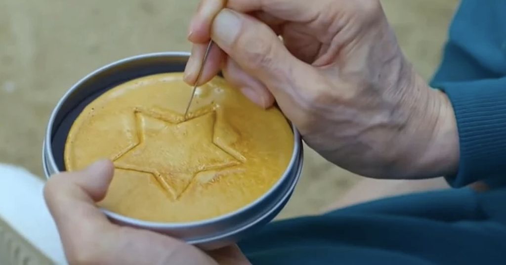 Oh Il-nam tenta di cesellare intatto il suo pezzo a nido d'ape in Squid Game.