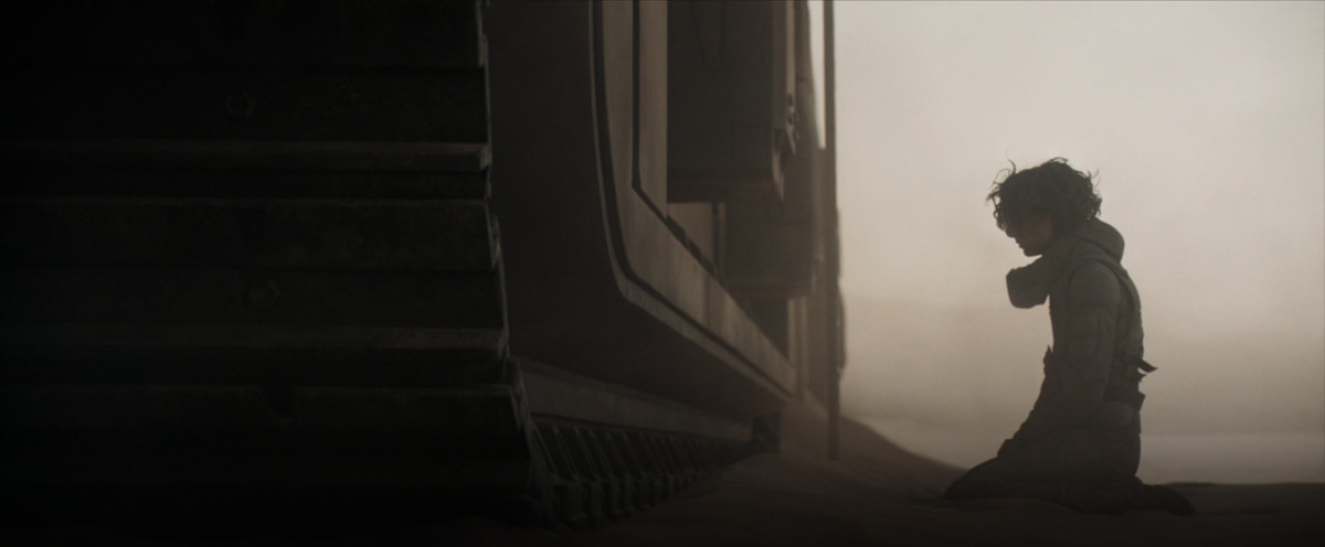 Paul Atreides si inginocchia alla base di un cingolato di sabbia in Dune (2021).