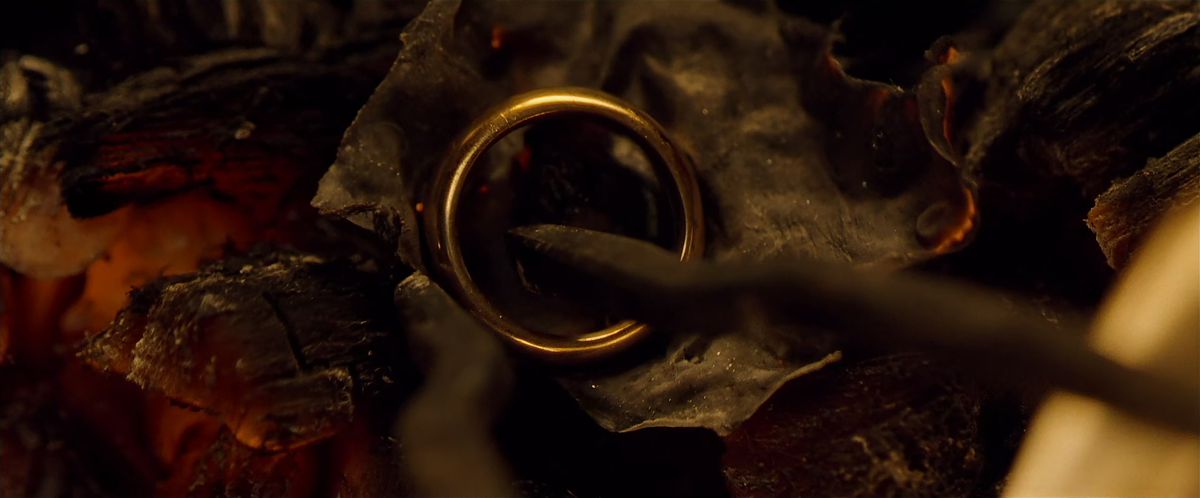 Tongs reach into the ashes of a fire to grasp the One Ring in The Fellowship of the Ring.