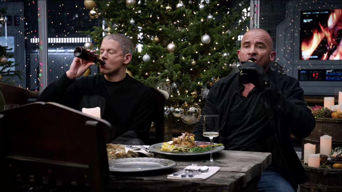 Captain Cold (Wentworth Miller) and Heat Wave (Dominic Purcell) knock back beers at the Christmas dinner table in Legends of Tomorrow.
