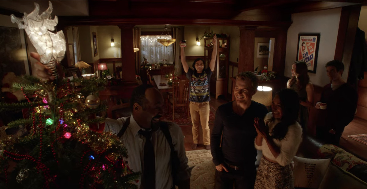 The West family celebrates Christmas with friends, cheering as Joe West (Jesse L. Martin) tops the family tree with an angel in The Flash.