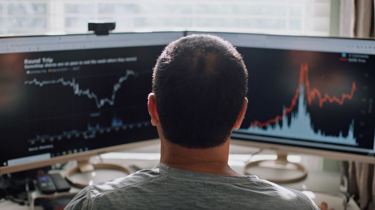 La parte posteriore della testa di un uomo mentre guarda due monitor di computer con i prezzi delle azioni in GameStop: Rise of the Players