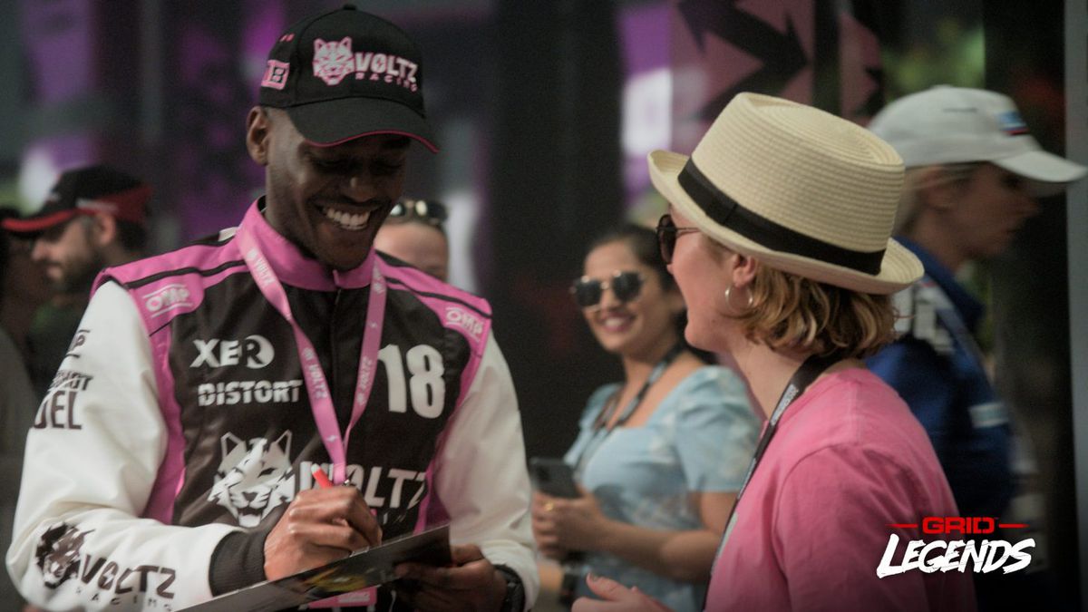 Un pilota, con indosso un berretto e un pass per il paddock, firma un autografo per un tifoso che indossa un cappello di paglia da barcaiolo
