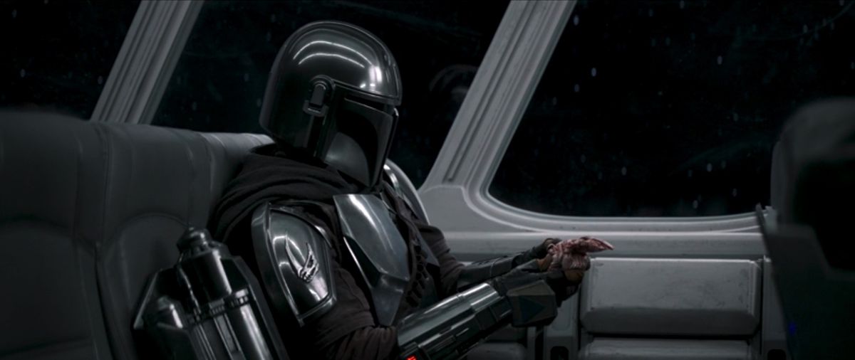 Il Mandaloriano tiene in mano una bambola Grogu di stoffa come un bravo papà