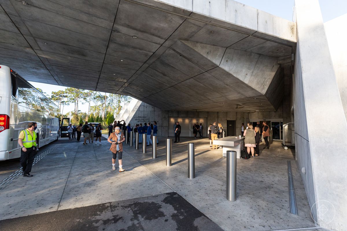 Dissuasori in acciaio bloccano la strada in un enorme bunker di cemento. Gli ospiti escono da un autobus in attesa.