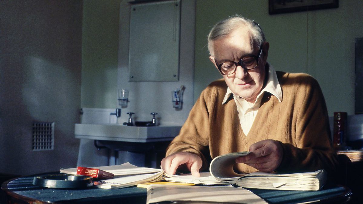 Alec Guinness nei panni di George Smiley che legge i giornali alla scrivania