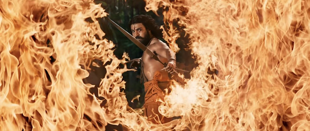 Un Jr NTR a torso nudo lancia una freccia attraverso una fessura in un muro di fuoco in RRR