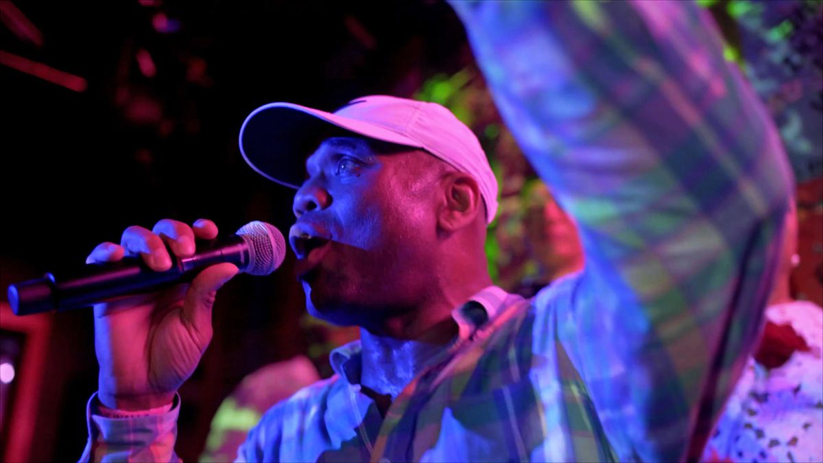 Un uomo in una sala da ballo parla in un microfono in Bring Down The Walls.