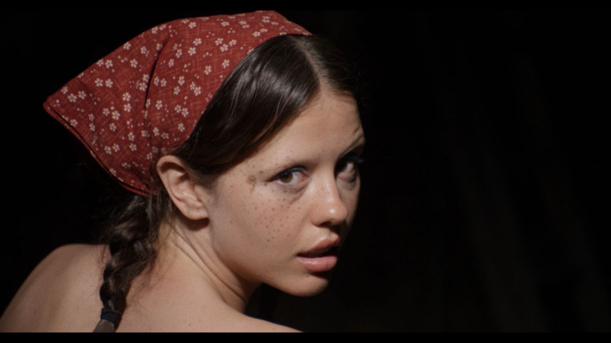 Mia Goth, con le spalle scoperte e la testa in un fazzoletto, lancia uno sguardo da dietro le sue spalle in X di Ti West
