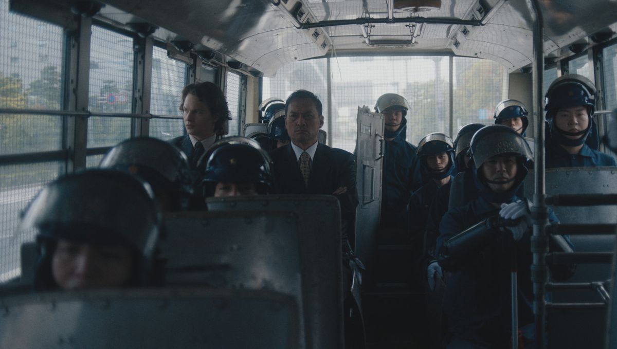 Ansel Elgort e Ken Watanabe nel retro di un autobus della polizia circondati da poliziotti in tenuta antisommossa nella serie HBO Max Tokyo Vice.