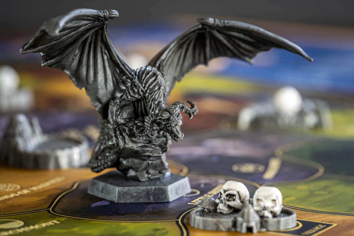 Una miniatura di drago incombe su una città, due teschi bianchi che riempiono la sua piazza.